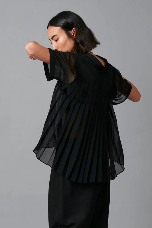Woman wearing a black outfit with sheer sleeves against a gray background
