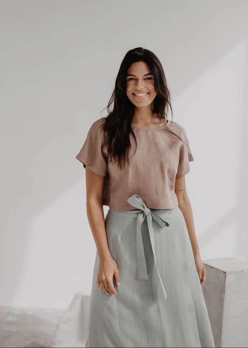 Woman wearing a beige top and light gray skirt against a white background