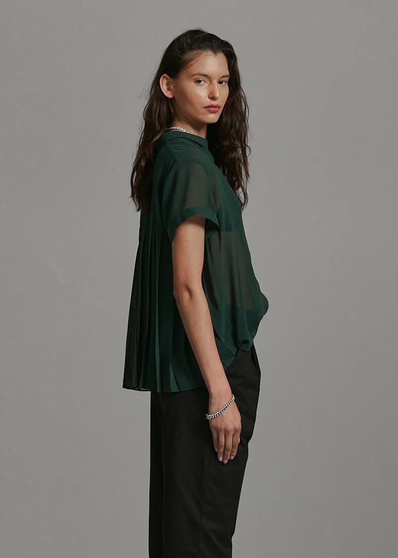 Woman wearing a green oversized t-shirt and black pants against a gray background