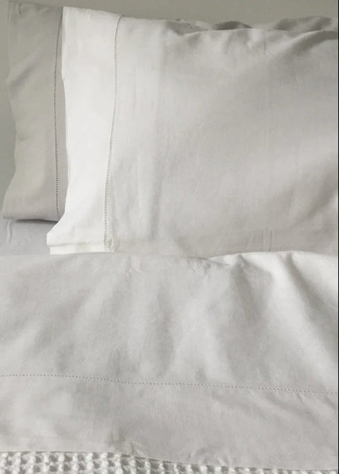 Close-up of light gray bedding with a pillow on a neutral background