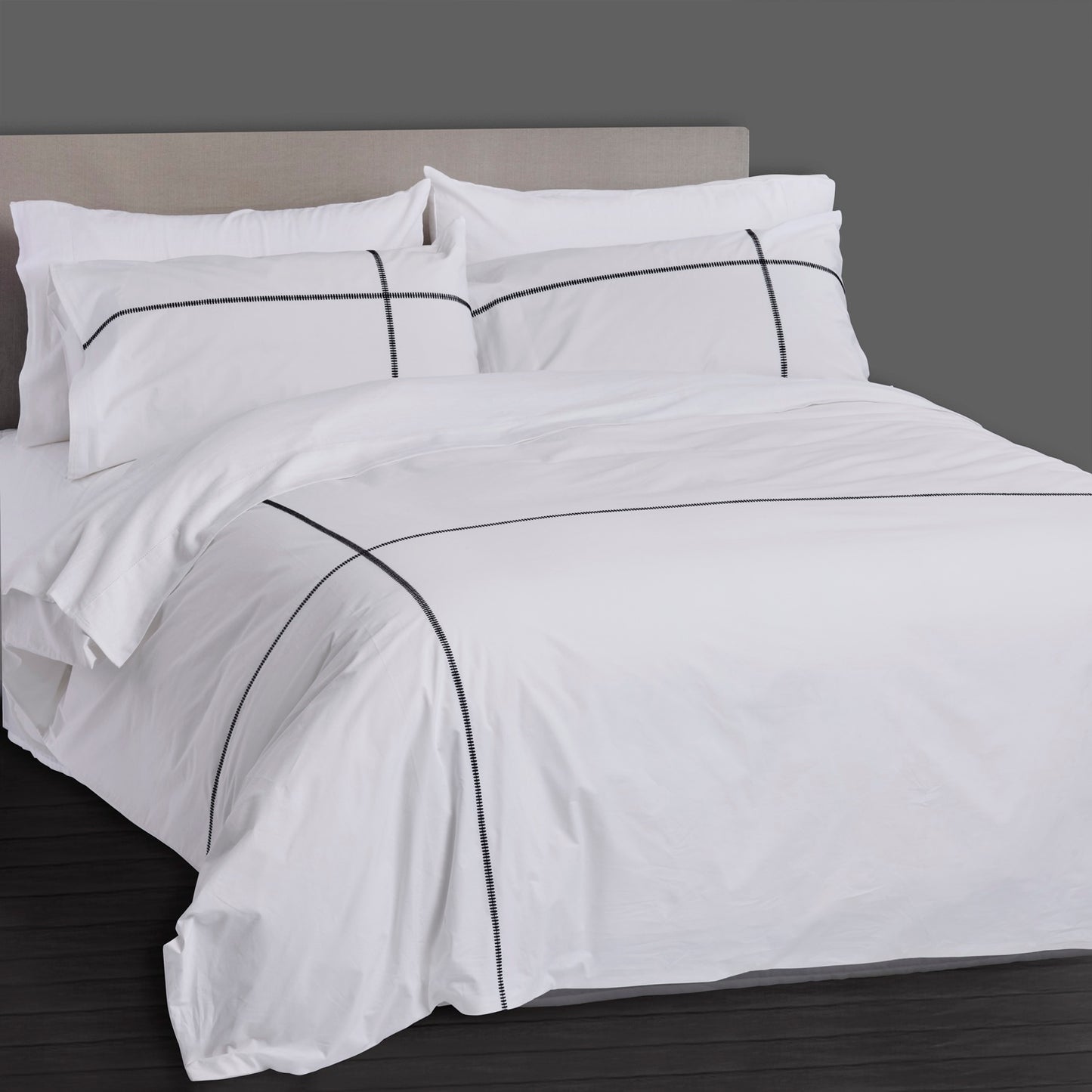 White bedspread with black piping on a bed against a gray background