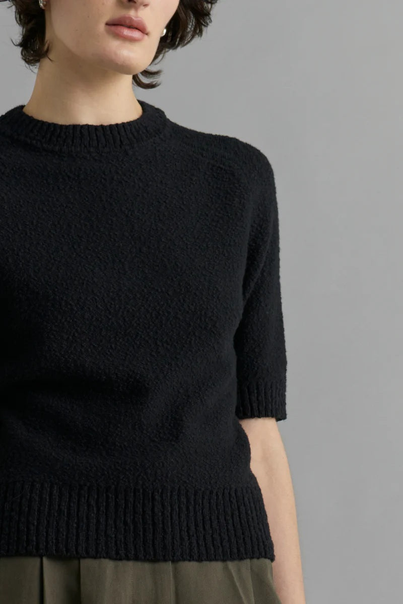 Person wearing a black knit sweater against a gray background