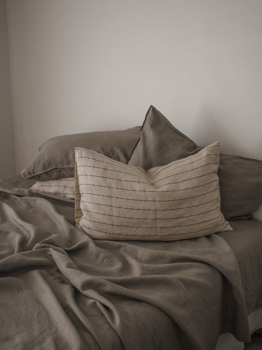 A Linen Duvet Cover in a muted green color, displayed on a bed with a pillow and a quilt, with a focus on the fabric texture and the cover's corner ties.