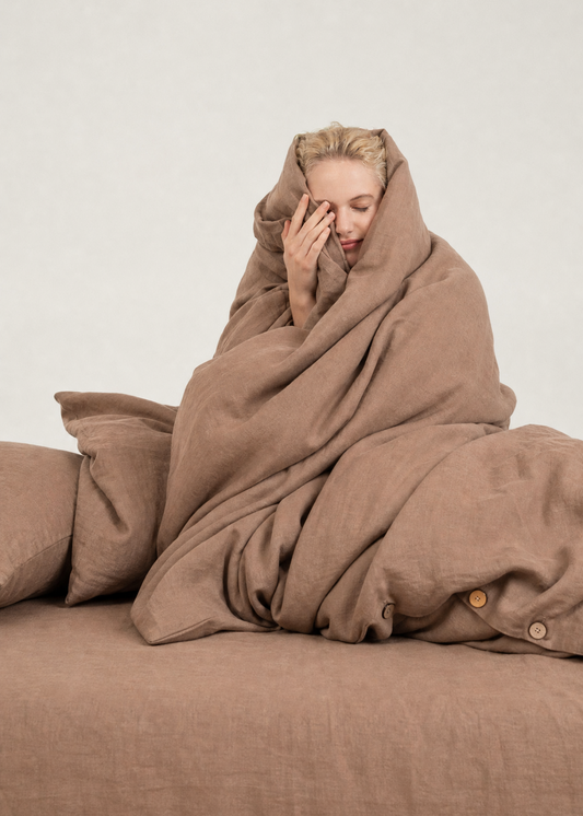 Person wrapped in a brown blanket on a couch against a plain background