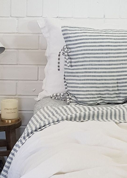 Bedroom with striped bedding, white lamp, and candle on a wooden stool against a white brick wall.