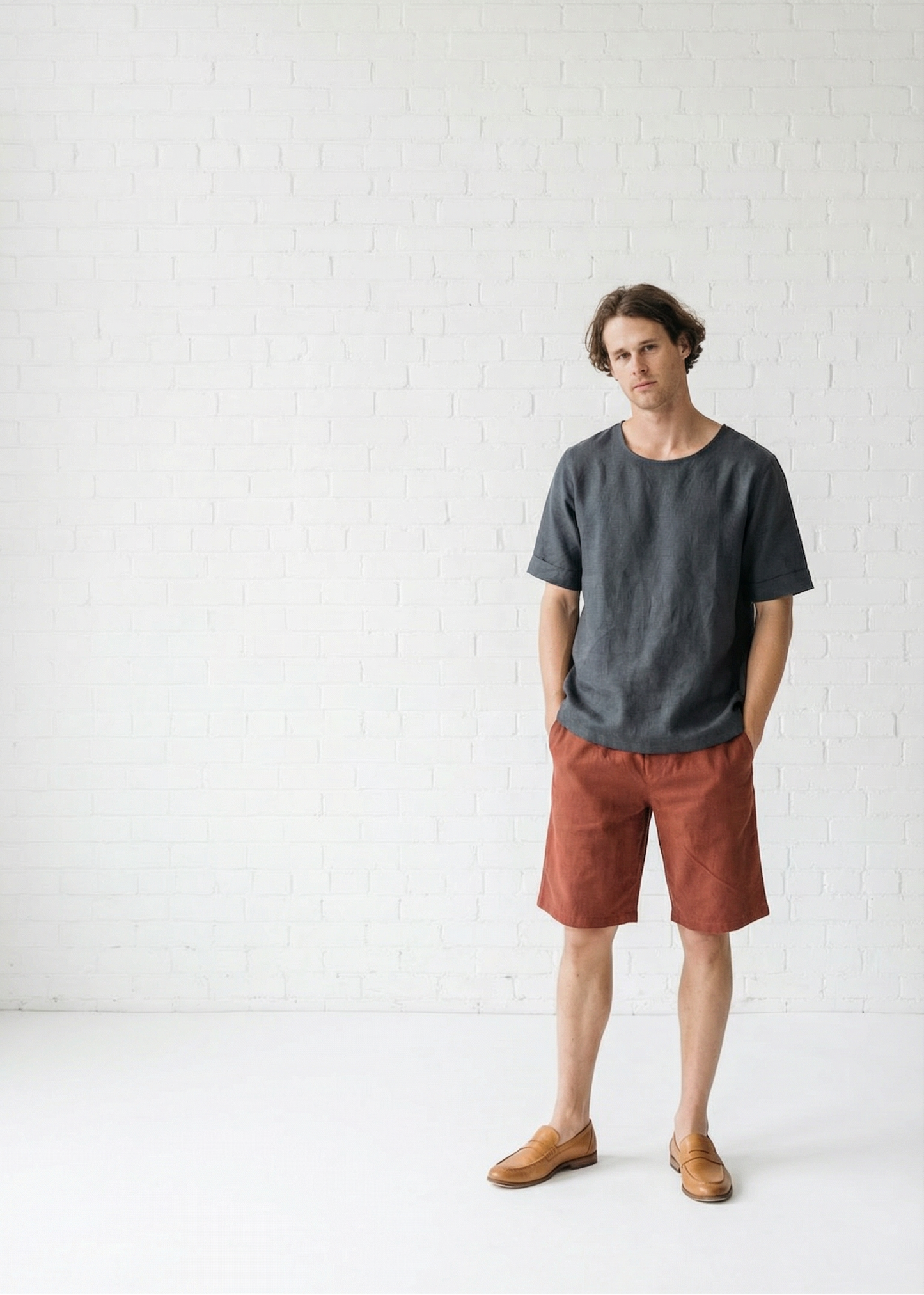 Man wearing a dark gray t-shirt and rust-colored shorts standing against a white background