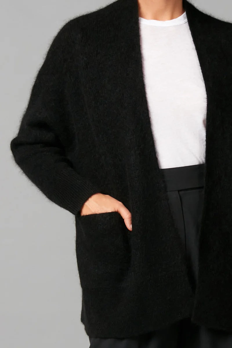 Person wearing a black coat with a white shirt and dark pants on a gray background