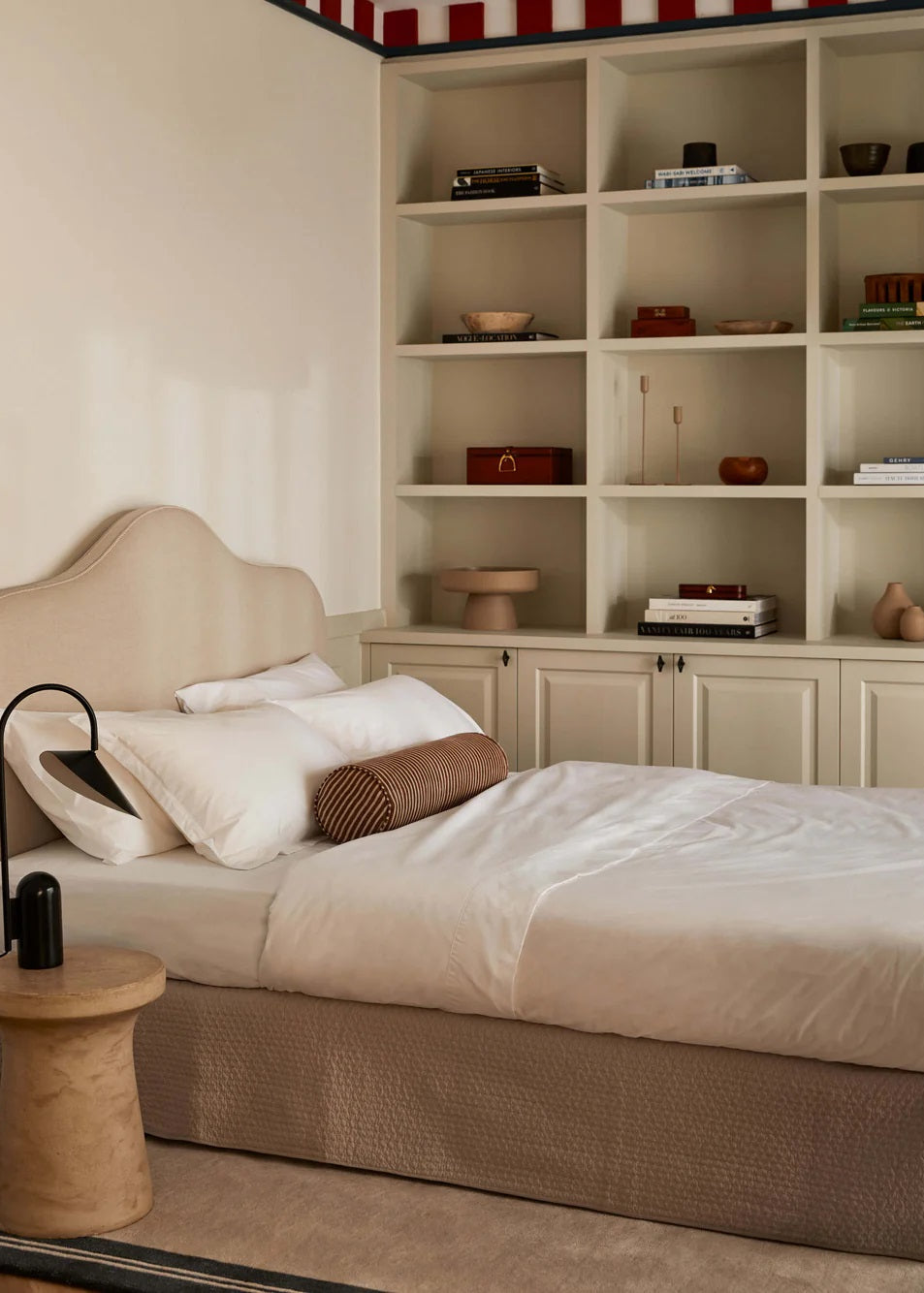 A made bed with a white flat sheet, pillowcases, and a quilt, placed in a room with a bookshelf and a lamp.