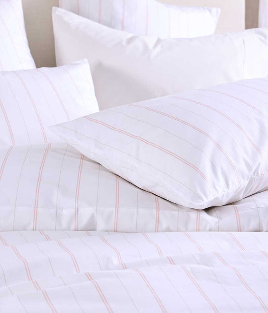 White bedding set with pink stripes on a bed.