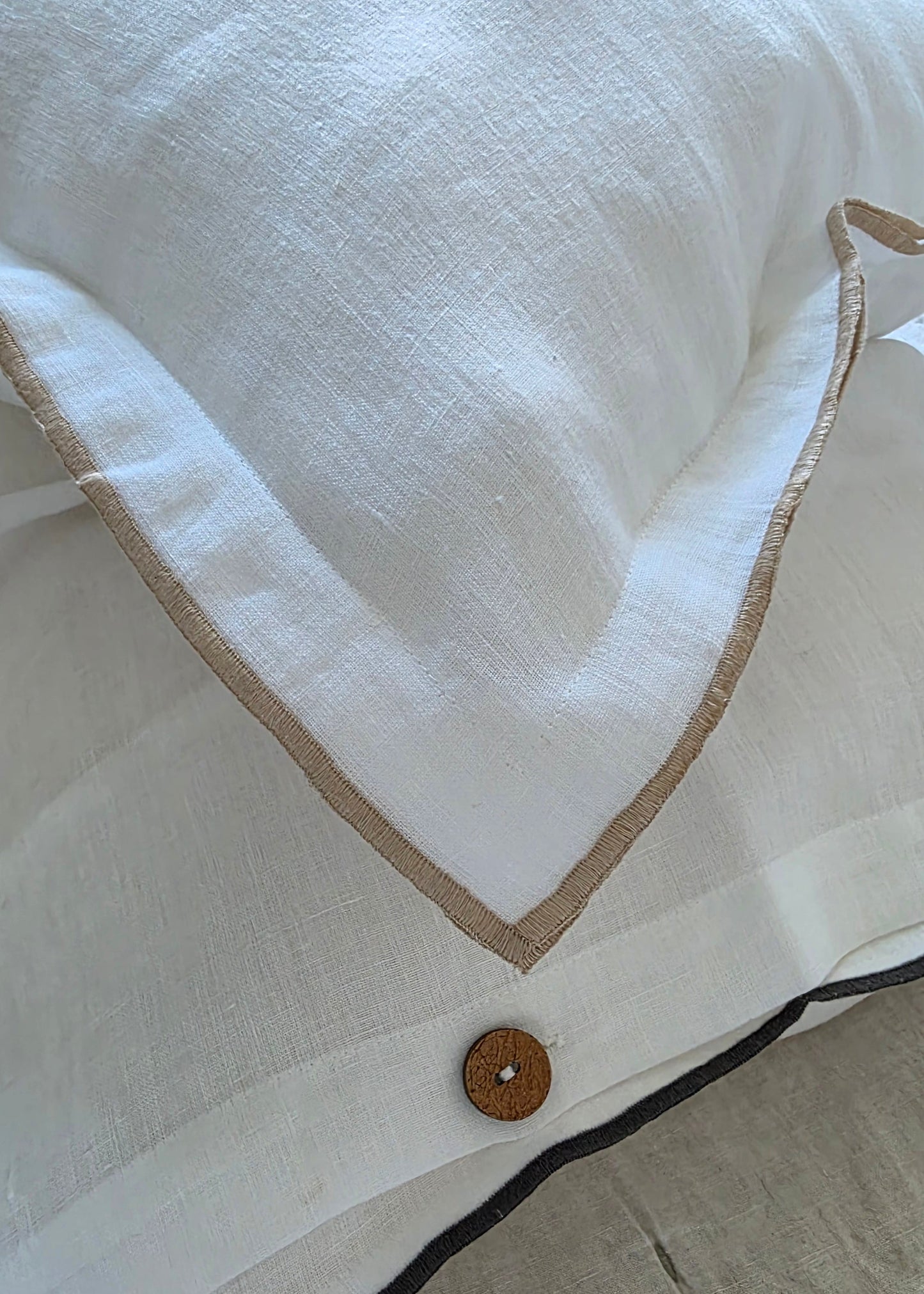 Close-up of a white shirt with a button and brown trim on a beige background