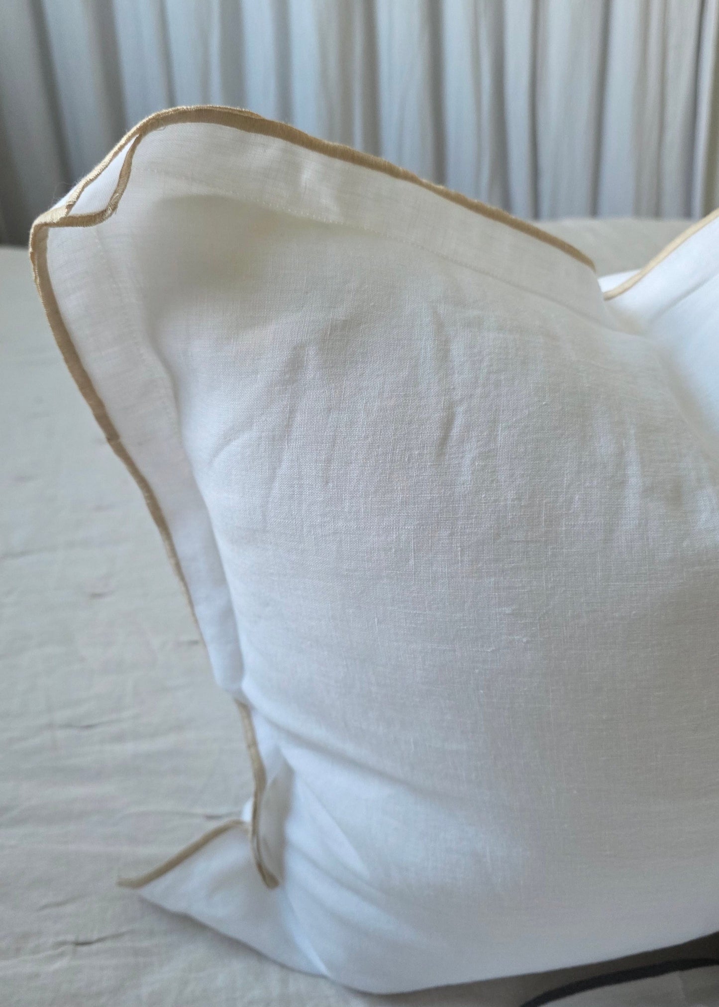 Close-up of a white pillow with gold trim against a neutral background
