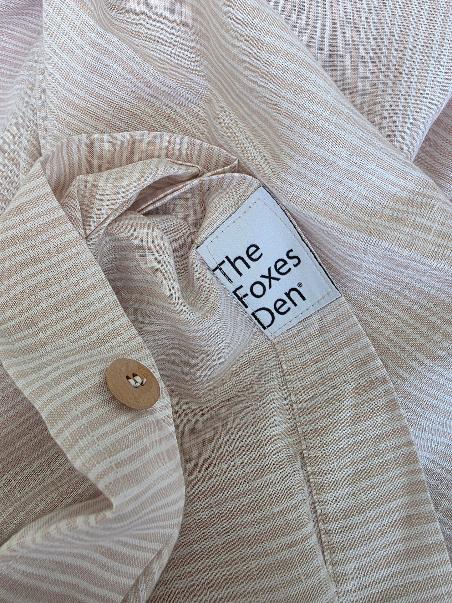 Close-up of a beige striped shirt with a label on the collar.