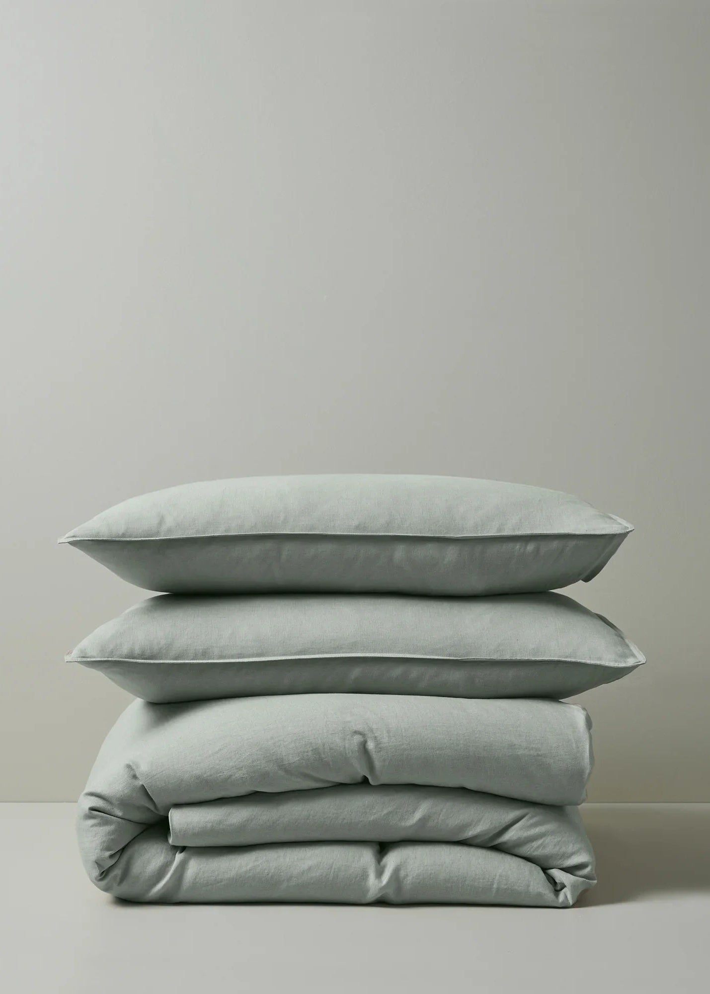 A stack of folded sage green linen pillowcases on a neutral background.