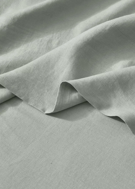 A close-up image of a flat linen sheet in a sage green color, displaying its woven texture and soft folds.