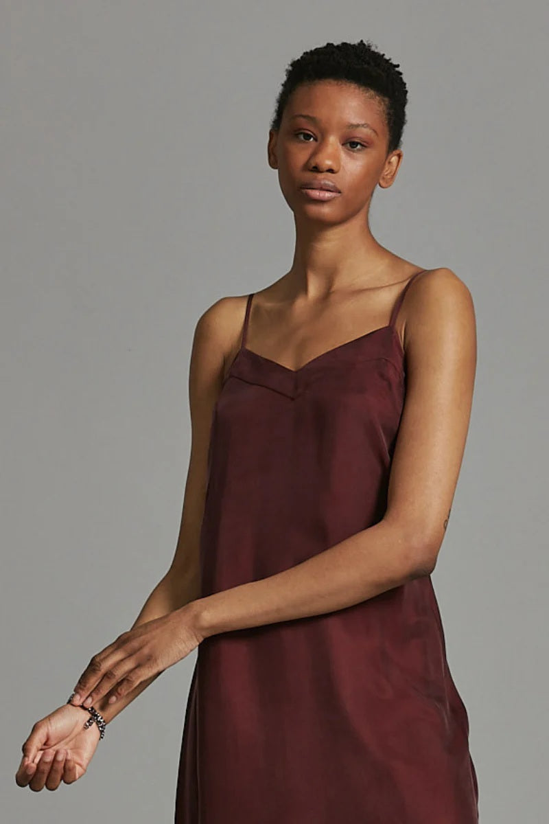 Woman wearing a burgundy slip dress against a gray background