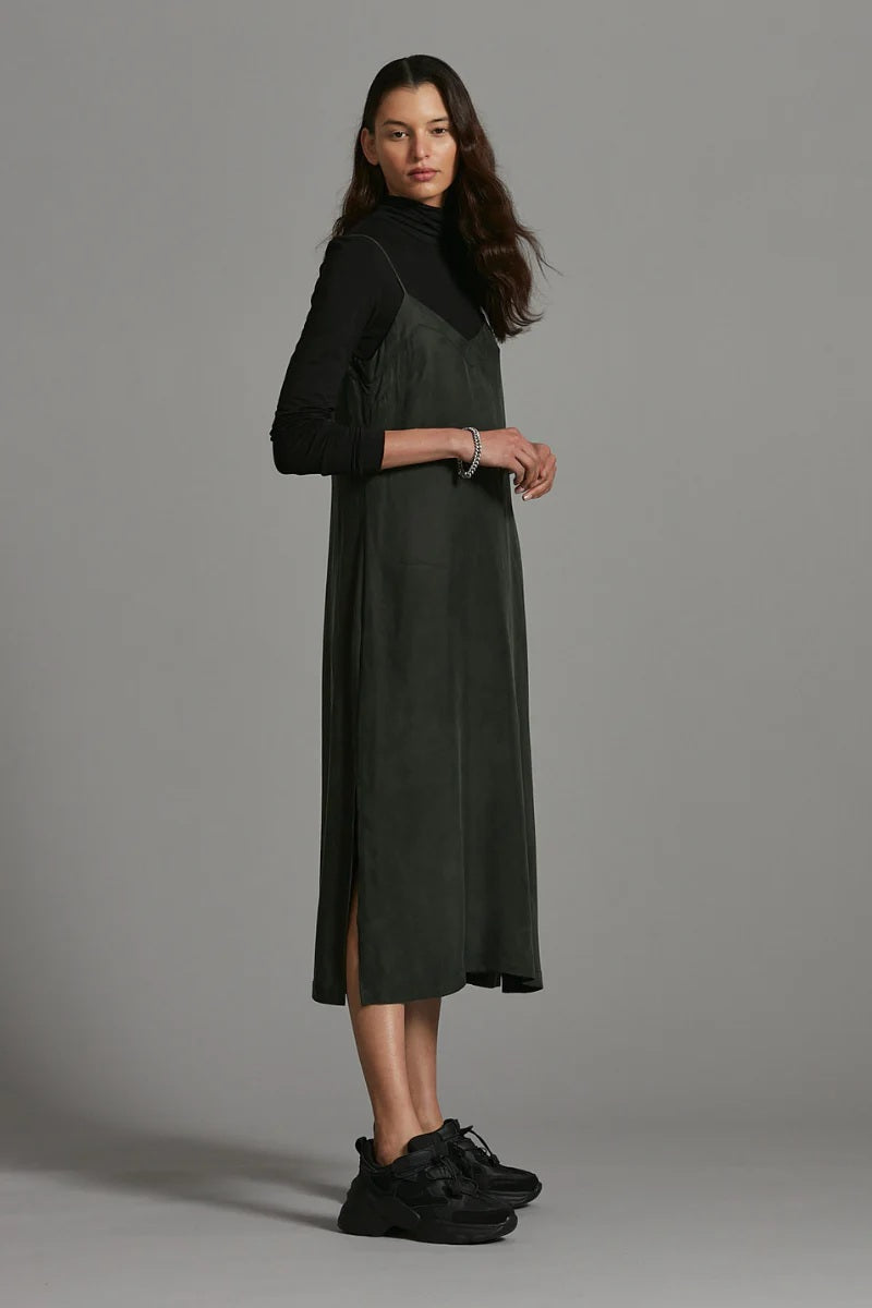 Woman wearing a dark green dress with a high collar against a gray background