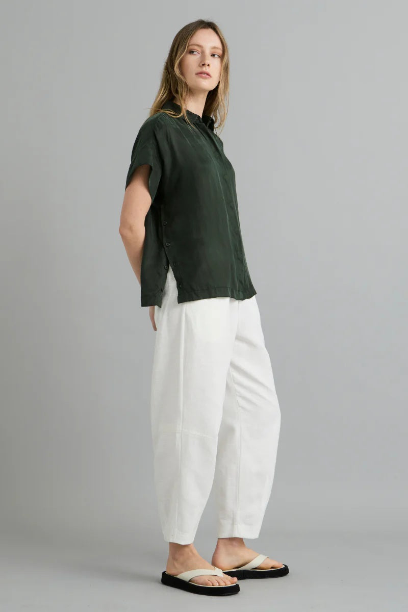 Woman wearing a green shirt and white pants on a gray background