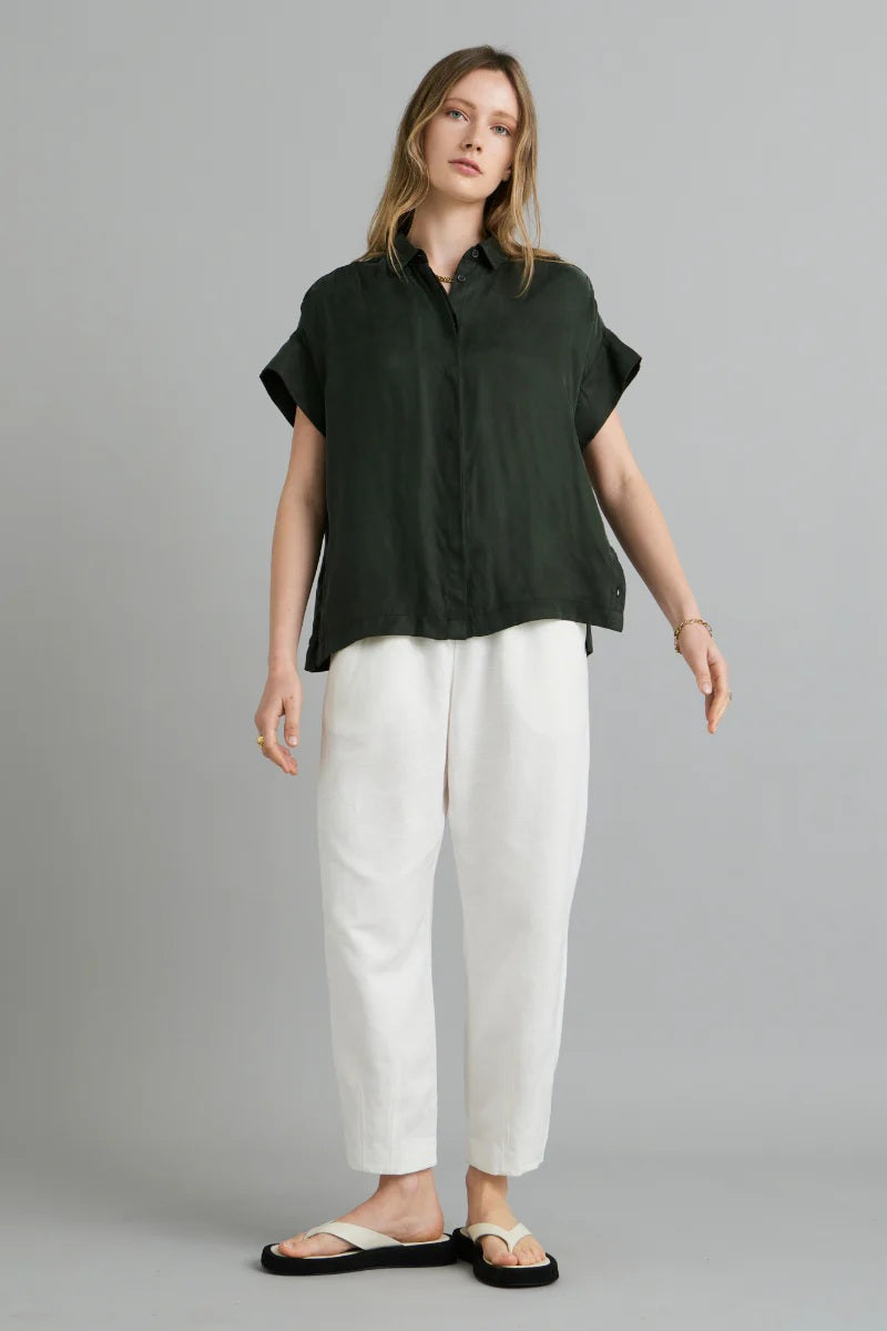 Woman wearing a dark green shirt and white pants on a gray background