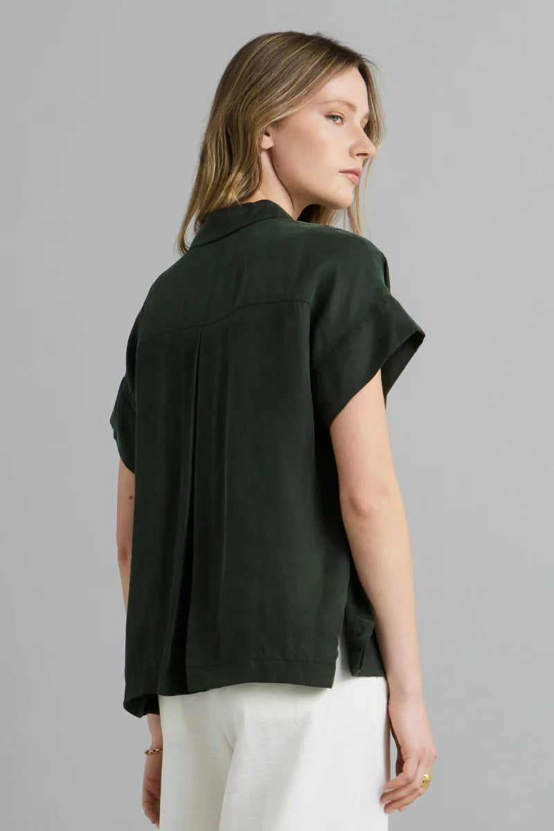 Woman wearing a dark green shirt and white pants on a gray background