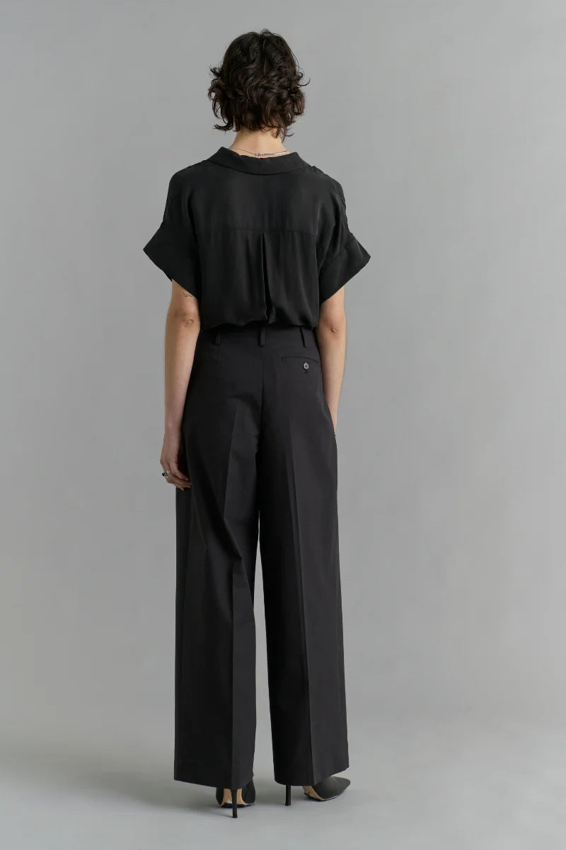 Person wearing a black outfit with wide-leg pants on a gray background