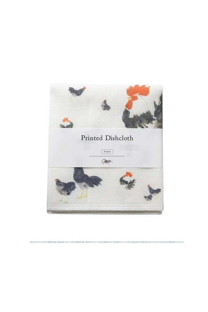 A dish cloth with a printed pattern featuring roosters and hens on a white background, packaged in a simple white and printed bag with the text 'DISH CLOTH' and 'Printed in Nara'.