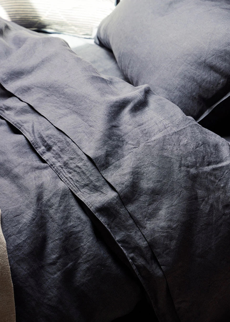 A close-up of a linen fitted sheet on a mattress, with a soft taupe color and a subtle texture.