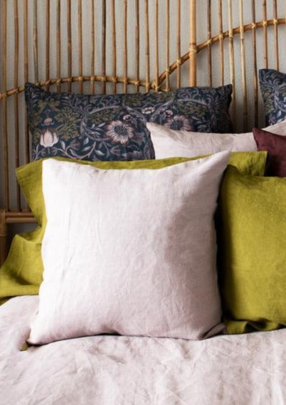 A dusky pink linen euro cover on a bed with other pillows and a wooden headboard in the background.