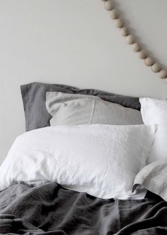 A pair of white linen pillowcases on a bed, with the pillowcases being the main focus.