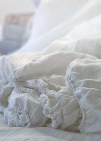 A folded pure white linen fitted sheet with elastic corners, showing a close-up of the linen fabric with a subtle texture.