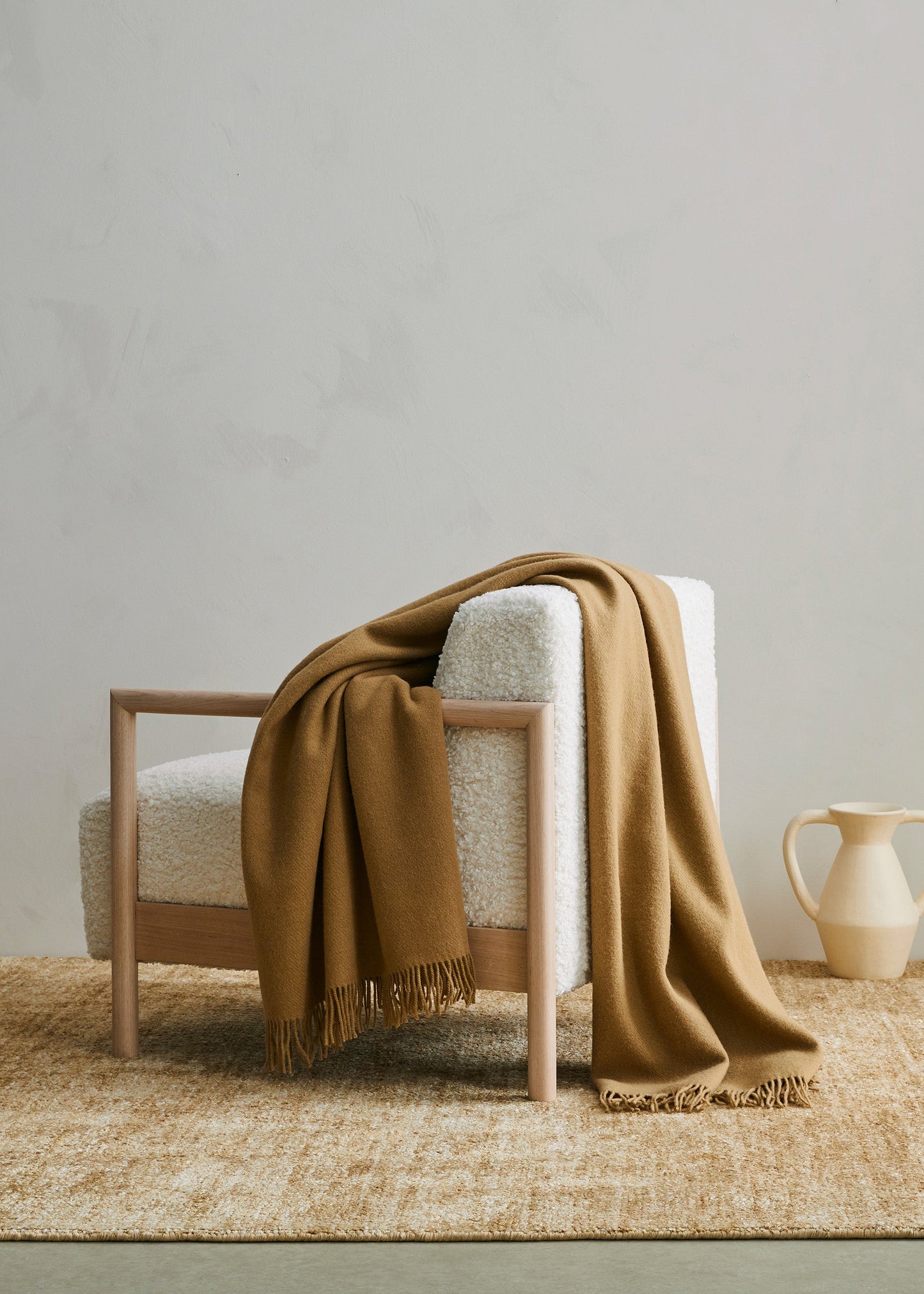 Chair with a brown blanket draped over it on a woven rug in a minimalistic room.