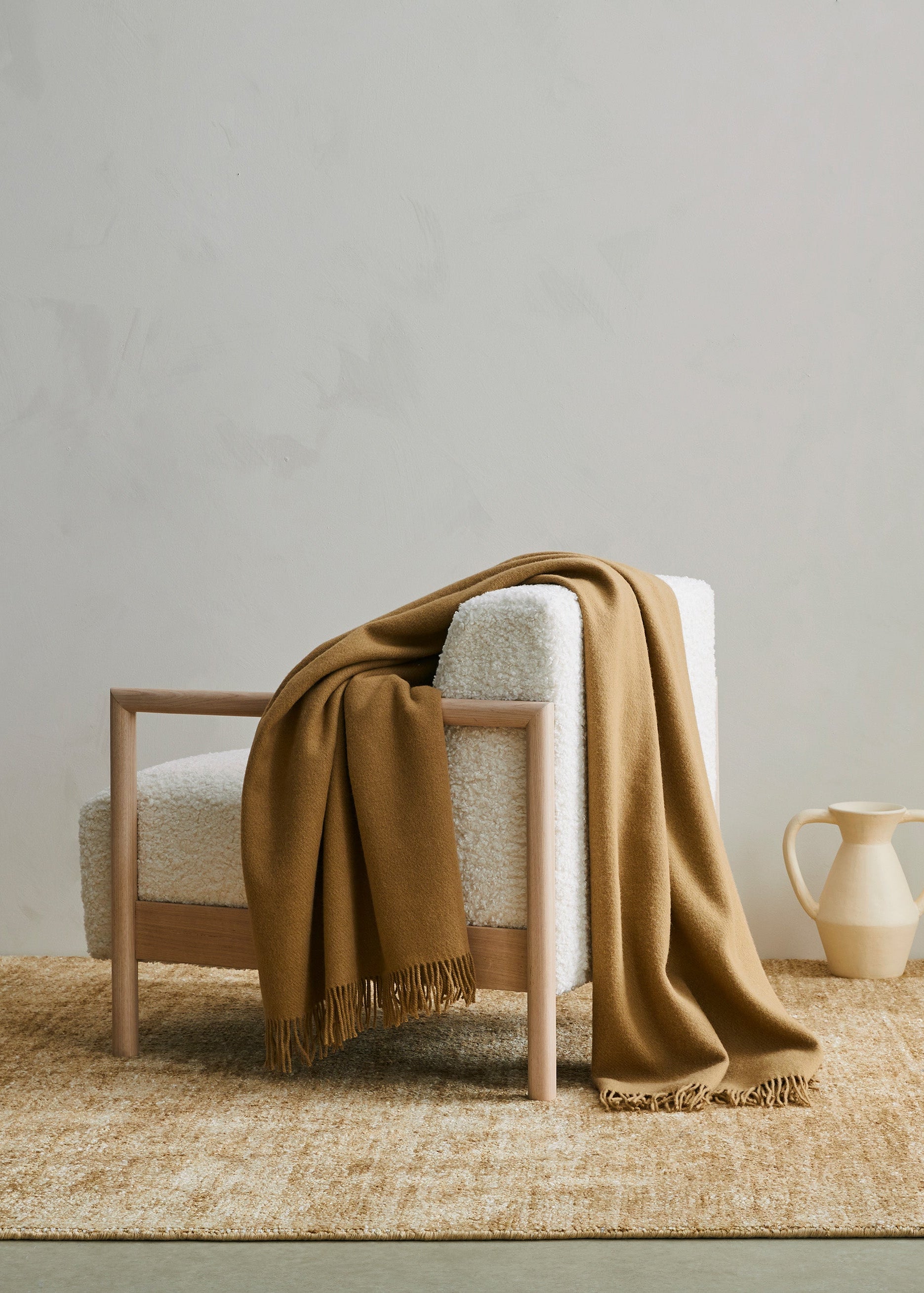 Chair with a brown blanket draped over it on a woven rug in a minimalistic room.