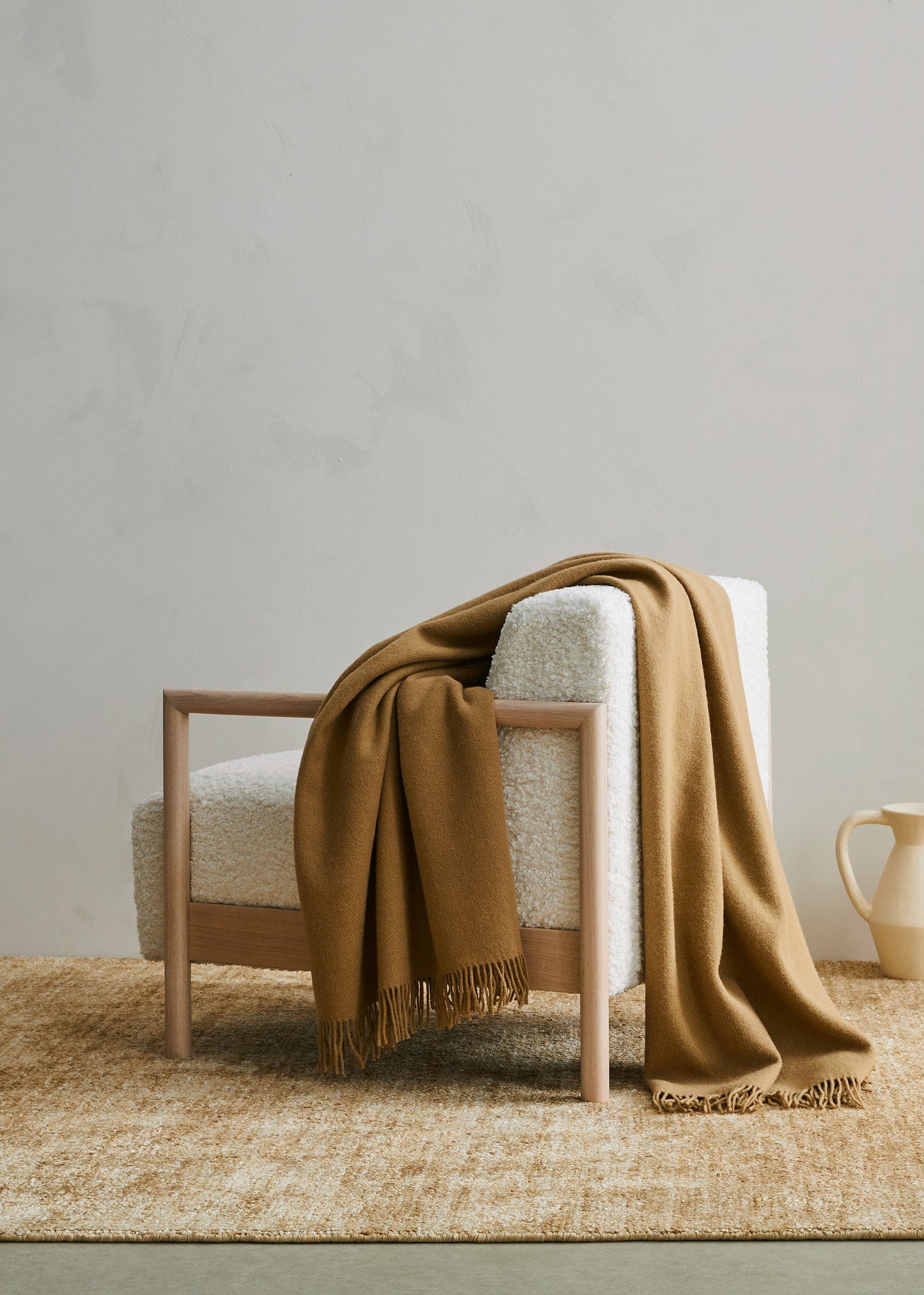 Chair with a brown blanket draped over it on a woven rug in a minimalistic room.