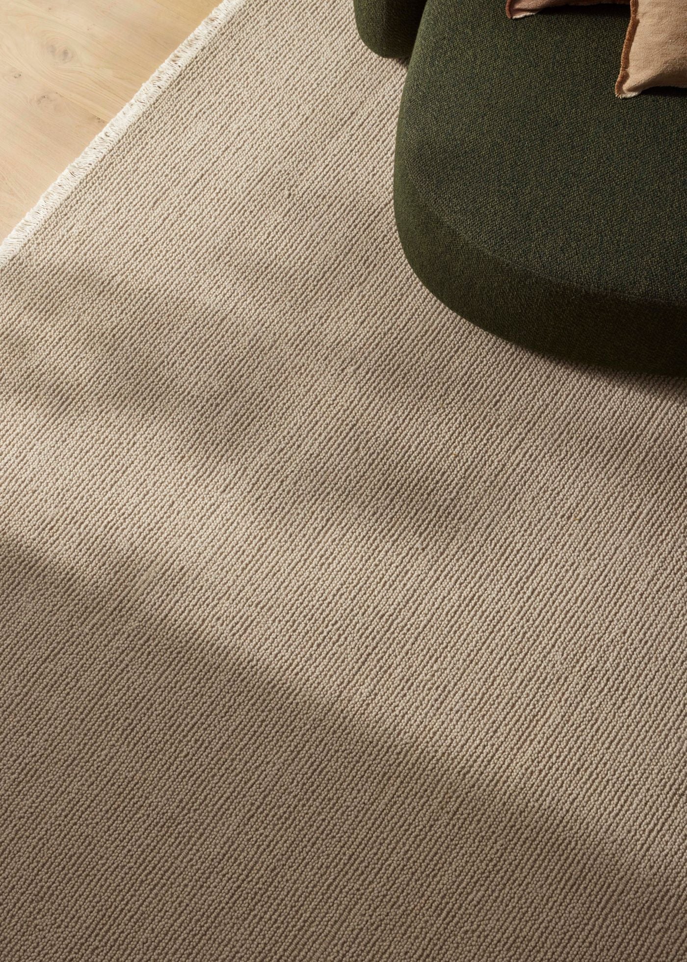 Close-up of a textured brown carpet with a green chair corner.