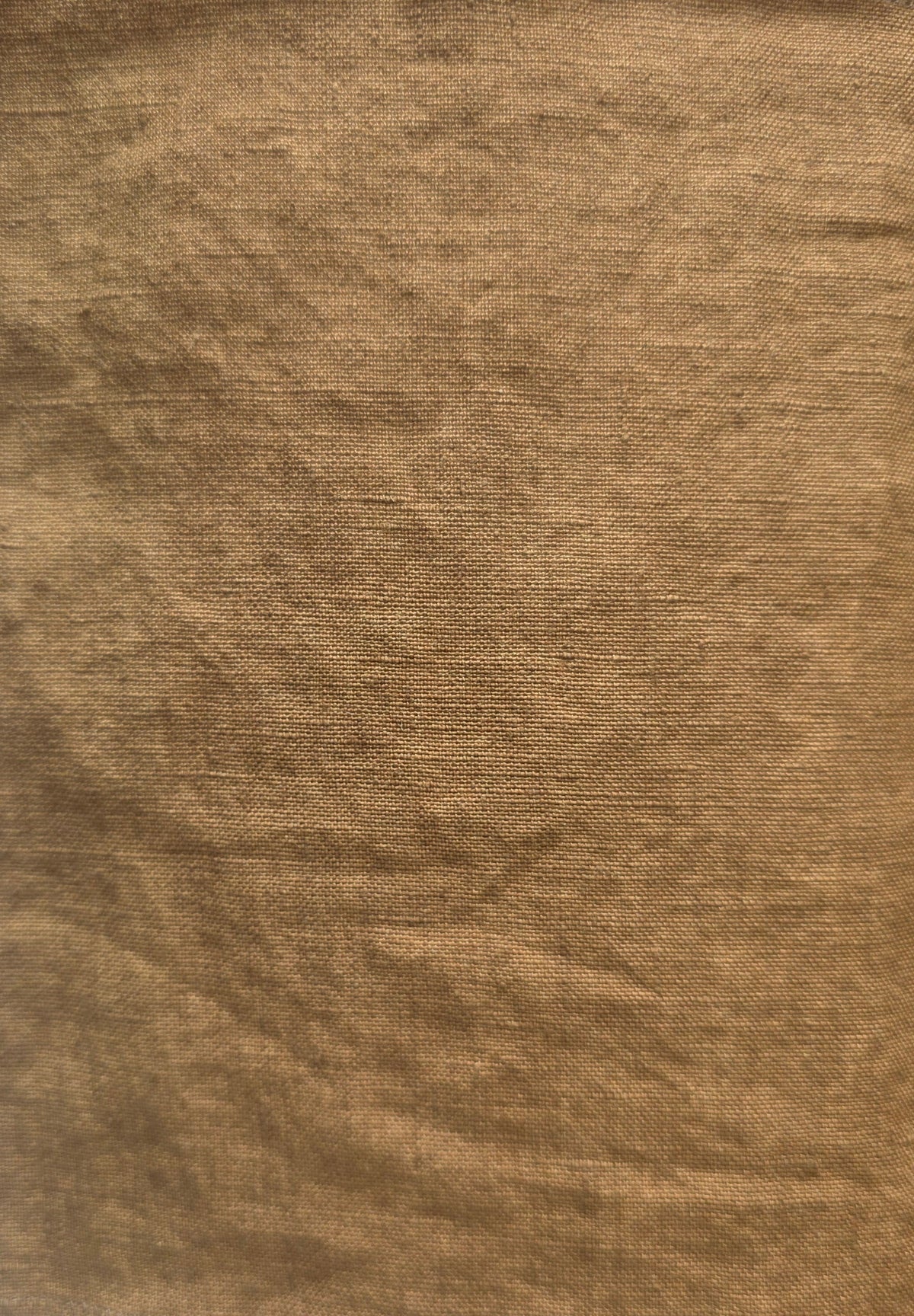 A square piece of textured tan fabric with frayed edges, laid flat on a white surface.