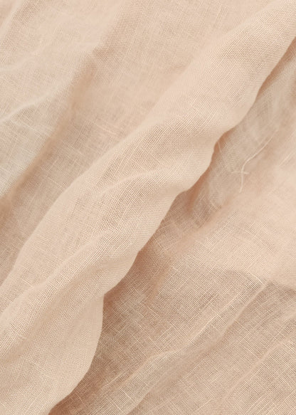 A close-up of draped, semi-sheer fabric in a light warm beige or blush tone, showing the soft texture and fine weave.
