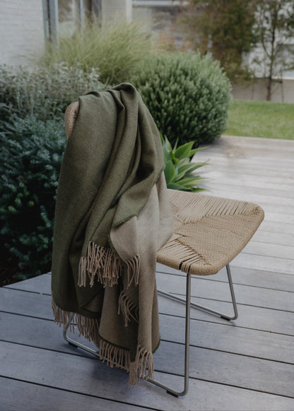 Green blanket draped over a chair on a wooden deck with greenery in the background