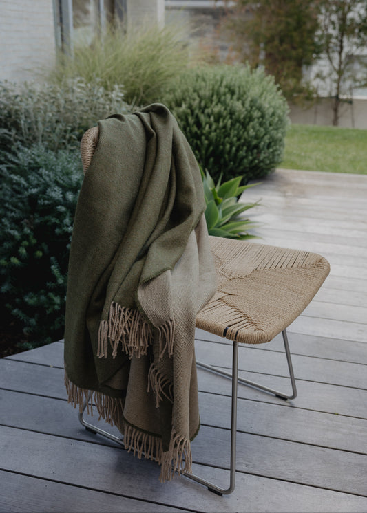 Green blanket draped over a chair on a wooden deck with greenery in the background