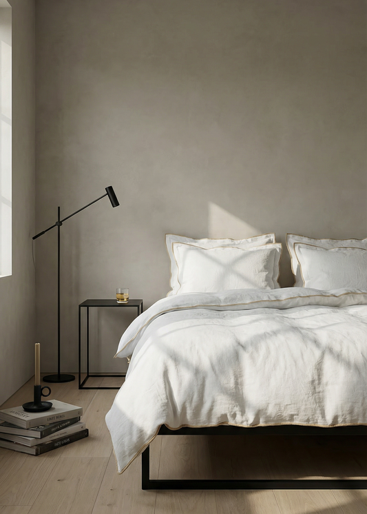 Minimalist bedroom with a bed, lamp, and side table against a plain wall.