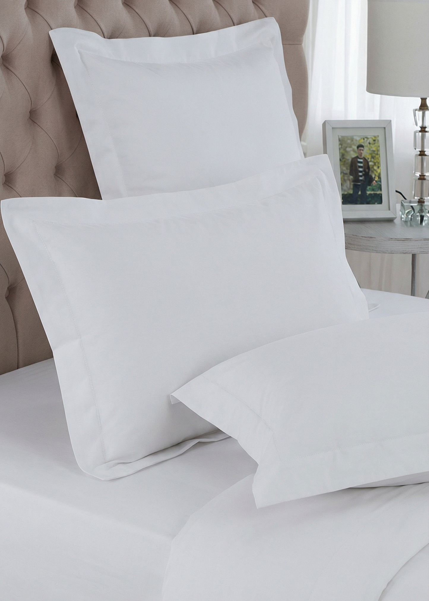 White pillows on a bed with a neutral headboard and lamp in the background