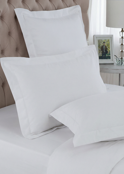 White pillows on a bed with a neutral headboard and lamp in the background