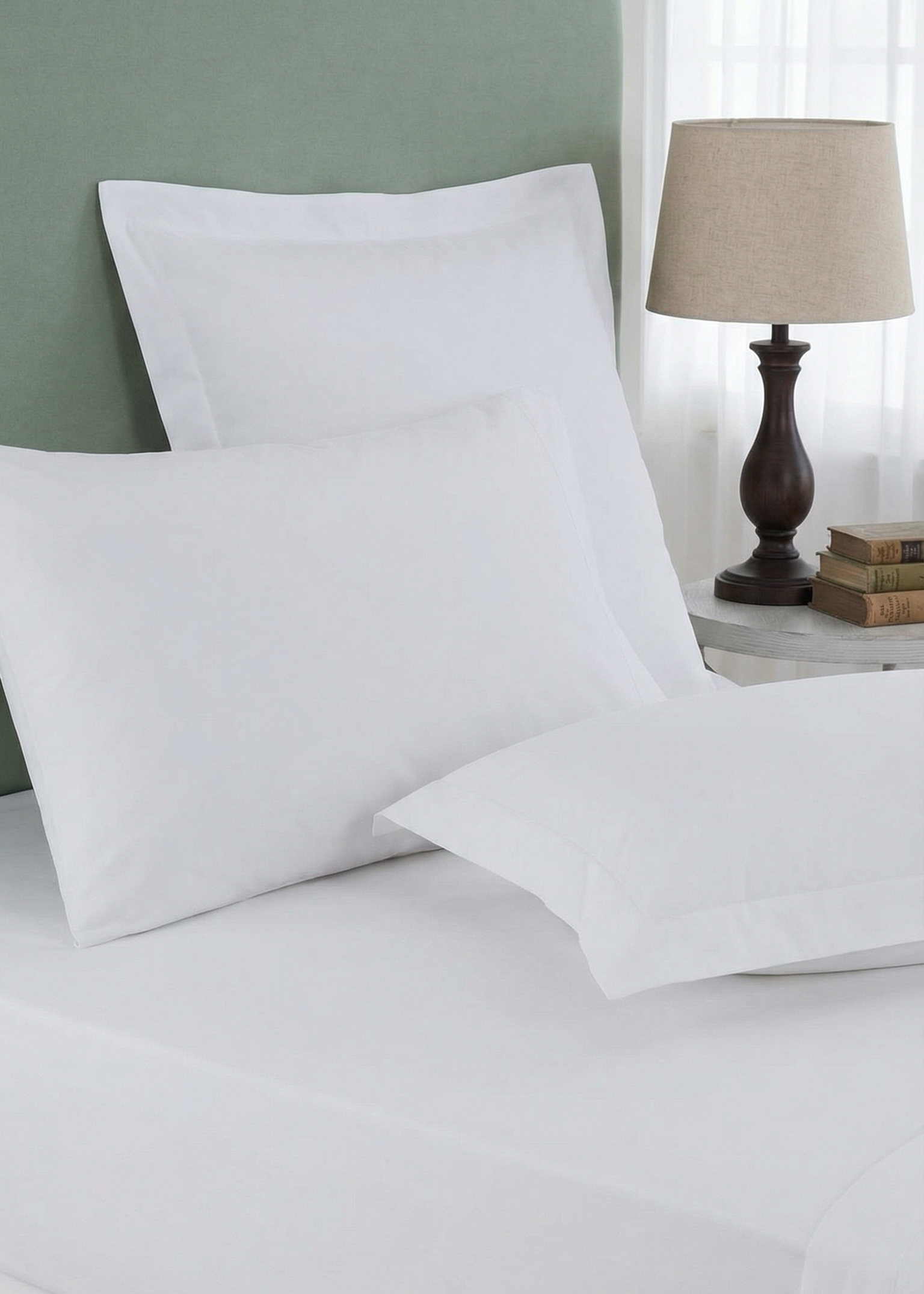 White pillows on a bed with a green headboard and lamp in the background