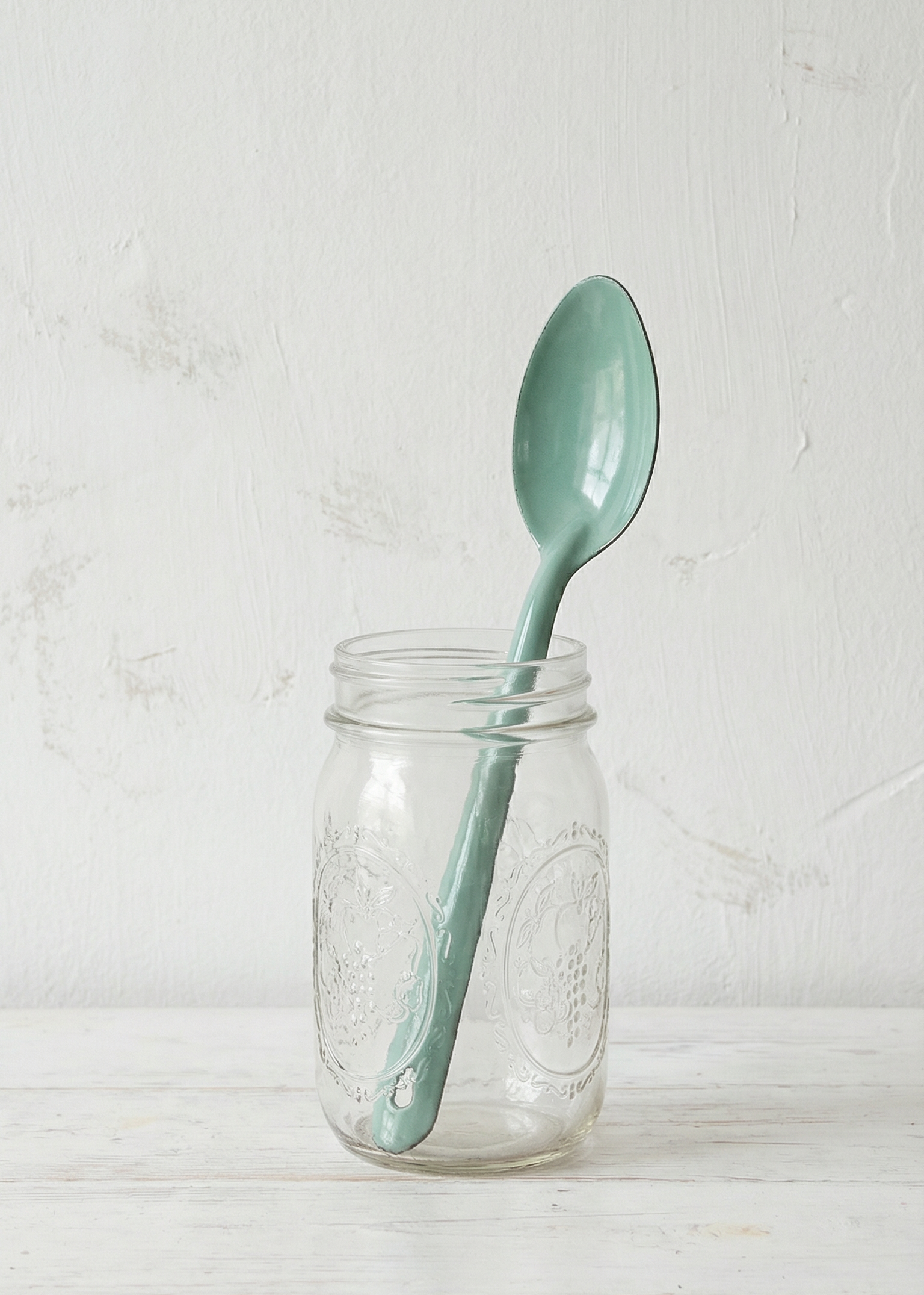 Light blue spoon inside a clear glass jar on a wooden surface with a white background