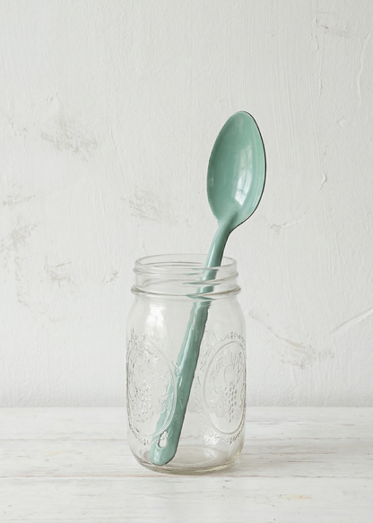 Light blue spoon inside a clear glass jar on a wooden surface with a white background