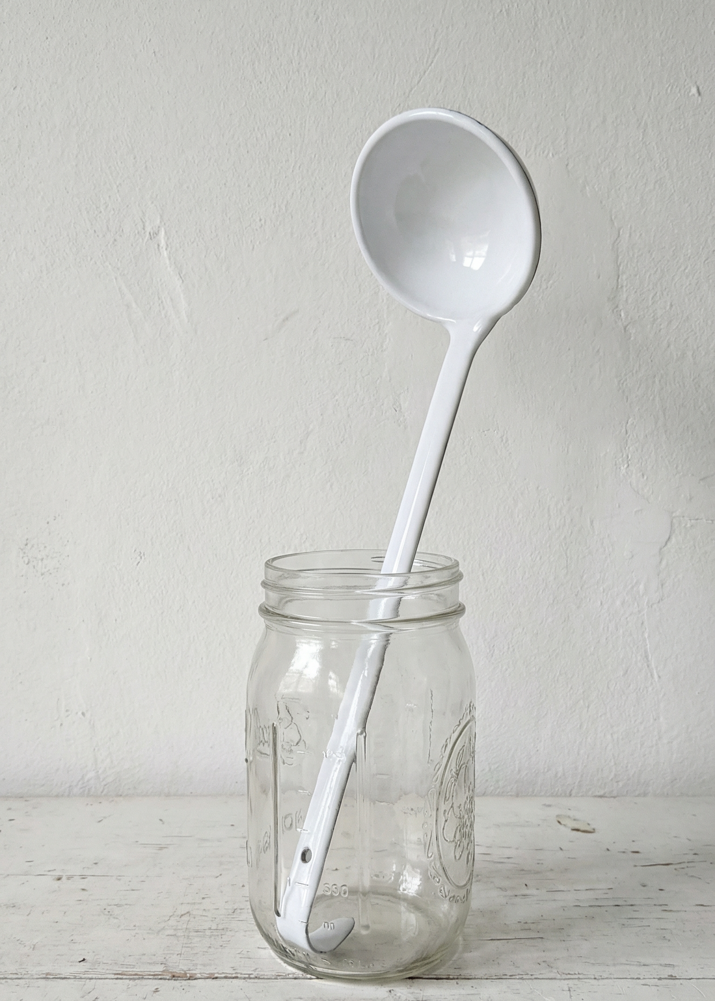 White ladle inside a clear glass jar on a light wooden surface with a white background