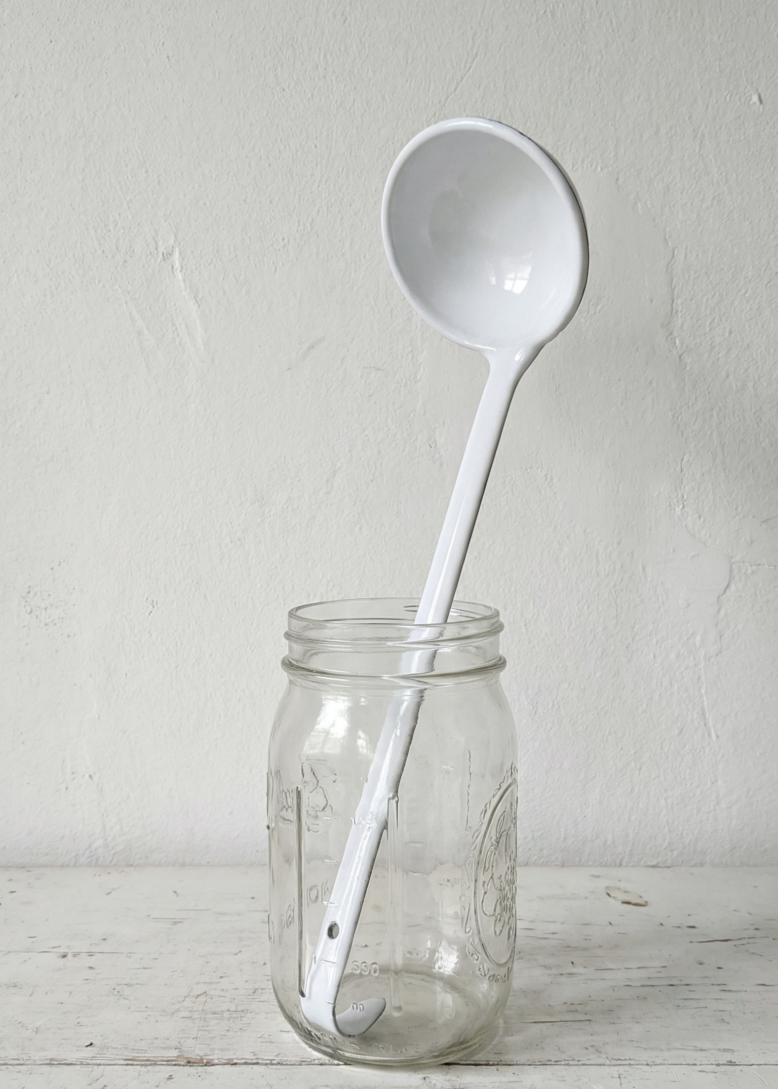 White ladle inside a clear glass jar on a light wooden surface with a white background