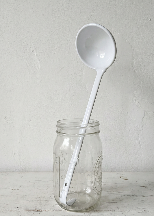 White ladle inside a clear glass jar on a light wooden surface with a white background