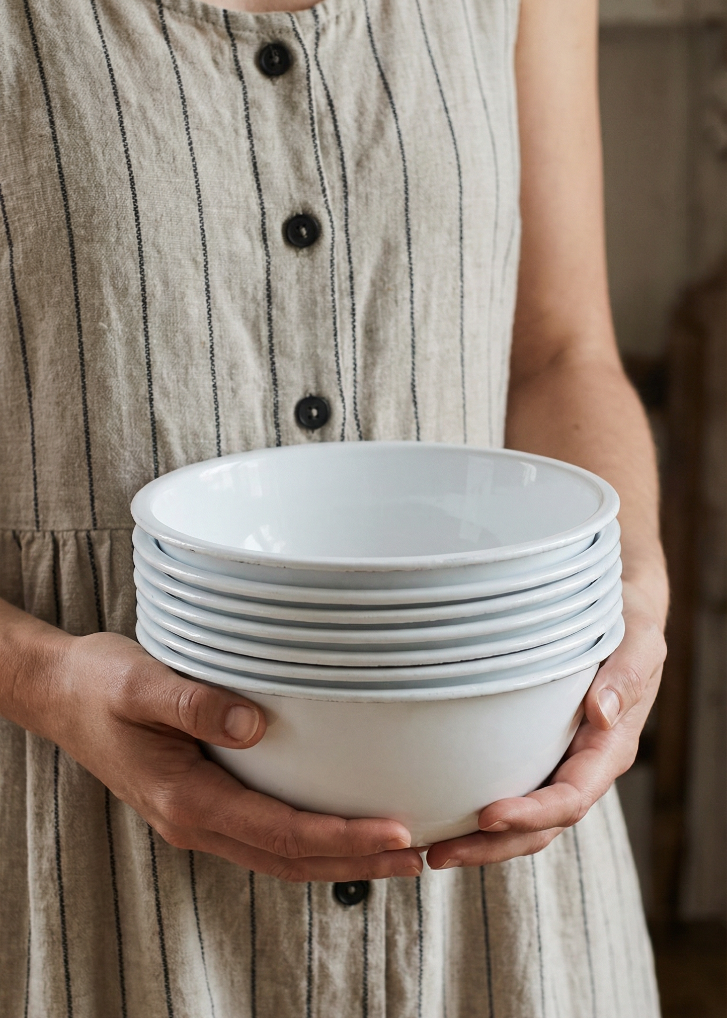 Person holding a stack of white ceramic bowls wearing a striped dress.