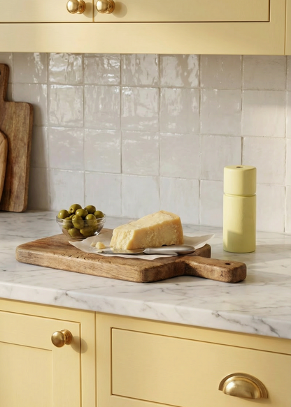 Kitchen counter with marble countertop, wooden cutting board, and yellow cabinets.