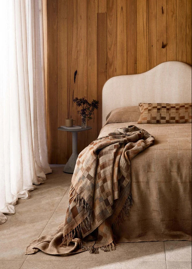 Bedroom with wooden wall, white curtains, and a bed with a plaid blanket.