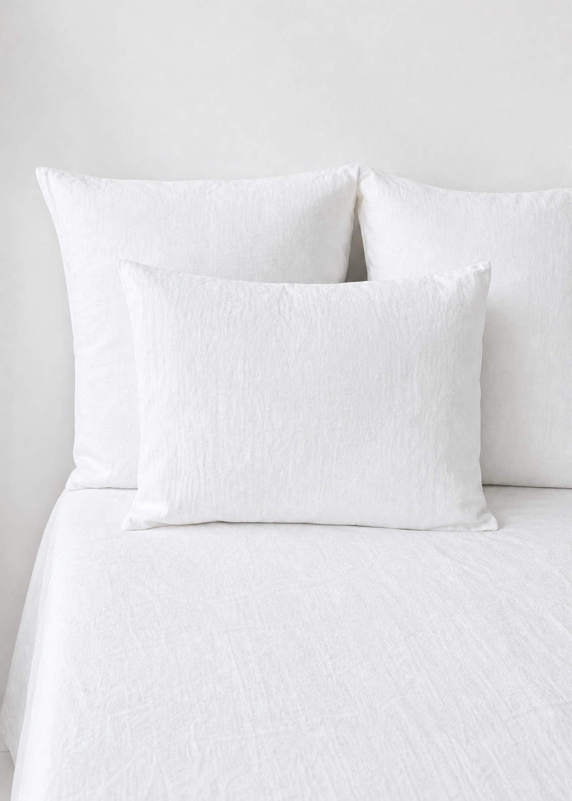 White textured bedding set with two large pillowcases and one smaller decorative pillow on a bed against a white wall.